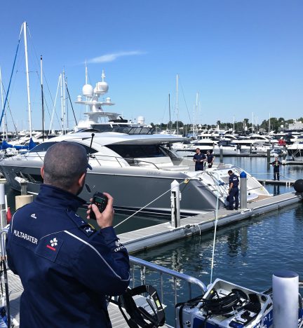 A crew member in uniform using a walkie-talkie while overseeing yacht docking procedures at a marina.