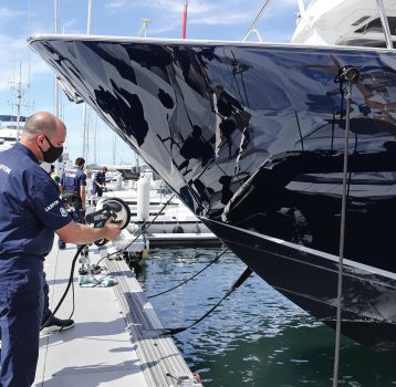 A marine professional is polishing a yacht's exterior for a high-gloss finish.