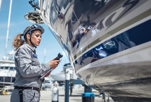 A marine surveyor inspecting a boat's fiberglass hull for cracks and imperfections, a critical part of Fiberglass Boat Repair to prevent future structural issues.
