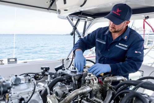 A marine technician in gloves and uniform fine-tunes a saltwater boat engine while docked at sea, ensuring proper saltwater boat engine maintenance.