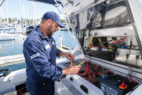 A marine technician in uniform examines battery wiring and voltage levels during boat battery testing and replacement.