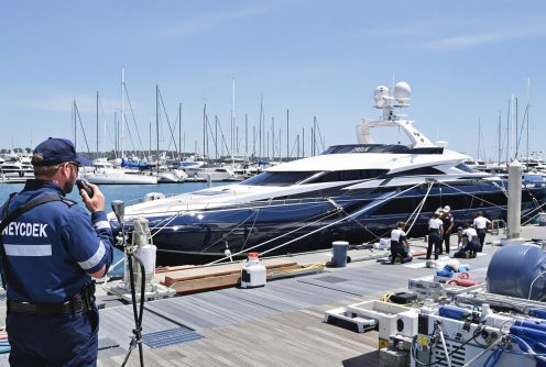 A security officer monitoring a luxury yacht mooring process at a busy dock.