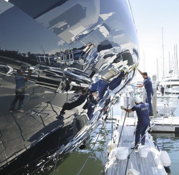 A team is performing detailed cleaning and maintenance on a luxury yacht’s hull.