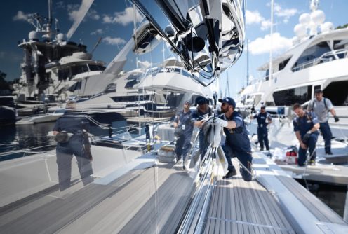 A team of technicians is detailing a yacht’s reflective exterior at a marina.