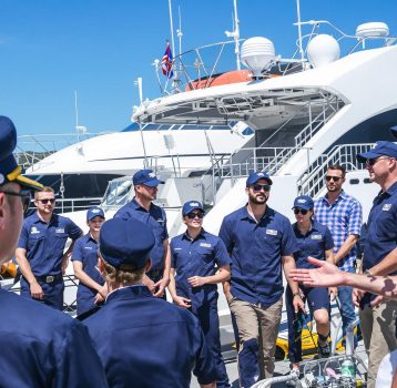 A team of yacht crew members being briefed before charter operations at a marina.
