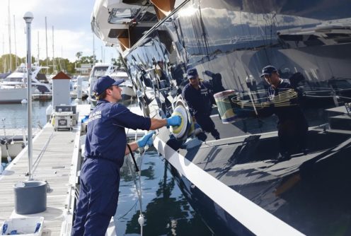 A worker is buffing and polishing the hull of a yacht to enhance its shine.