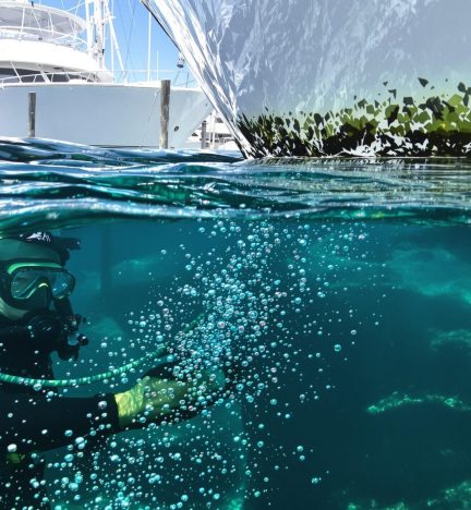 A diver uses a scraping tool to remove barnacle accumulation. Barnacle Removal and Hull Cleaning guarantees smooth sailing.