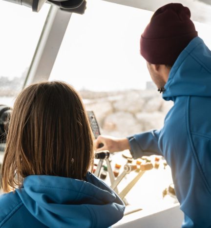 A captain guiding a child on a boat’s navigation system. A captain guiding a child on a boat’s navigation system.