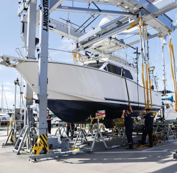 A sleek boat being lifted at a busy marina with spectators watching. Dry Dock and Haul-Out Services offers top-tier handling for all vessel sizes.