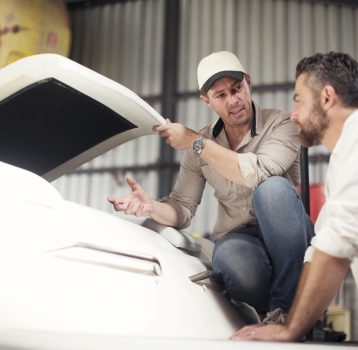 Two men checking boat bodywork in repair workshop