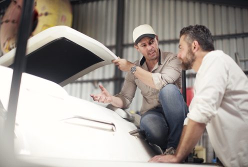 Two men checking boat bodywork in repair workshop